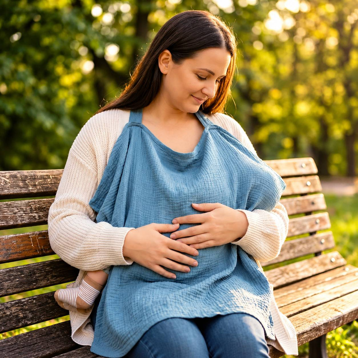 Cape d'allaitement bleue utilisée par une maman avec bébé assise dans un parc