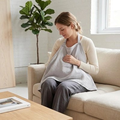 Cape d'allaitement portée par une maman assise avec bébé près d'une fenêtre