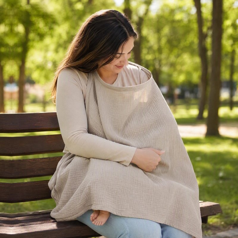 Cape d'allaitement beige utilisée par une maman avec bébé sur un banc au parc