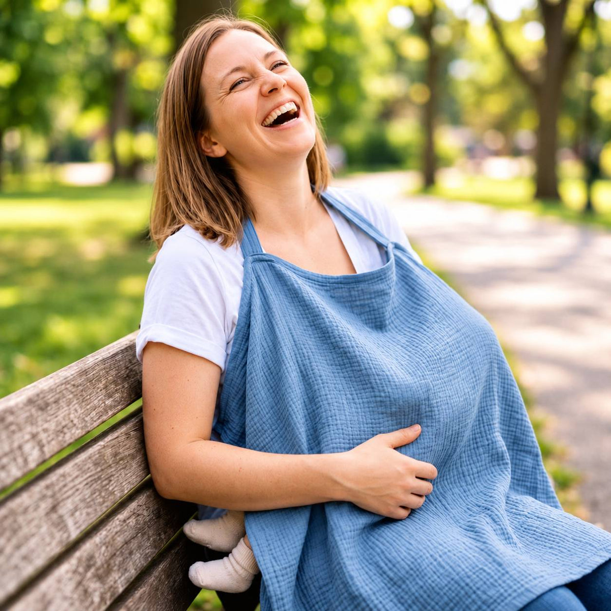 Maman utilisant une cape d'allaitement bleue avec bébé lors d'une pause au parc