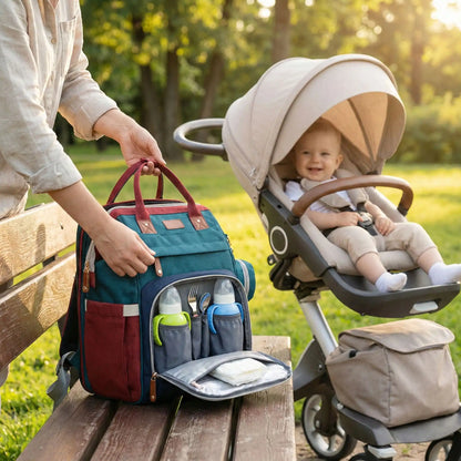 Une maman est au parc avec son bebe et un sac a langer avec berceau integre ou biberons sont visibles