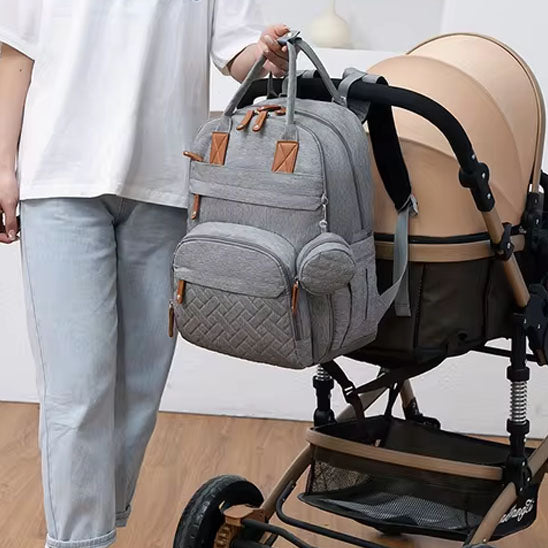 sac a dos a langer bebe gris accroche a une poussette en exterieur