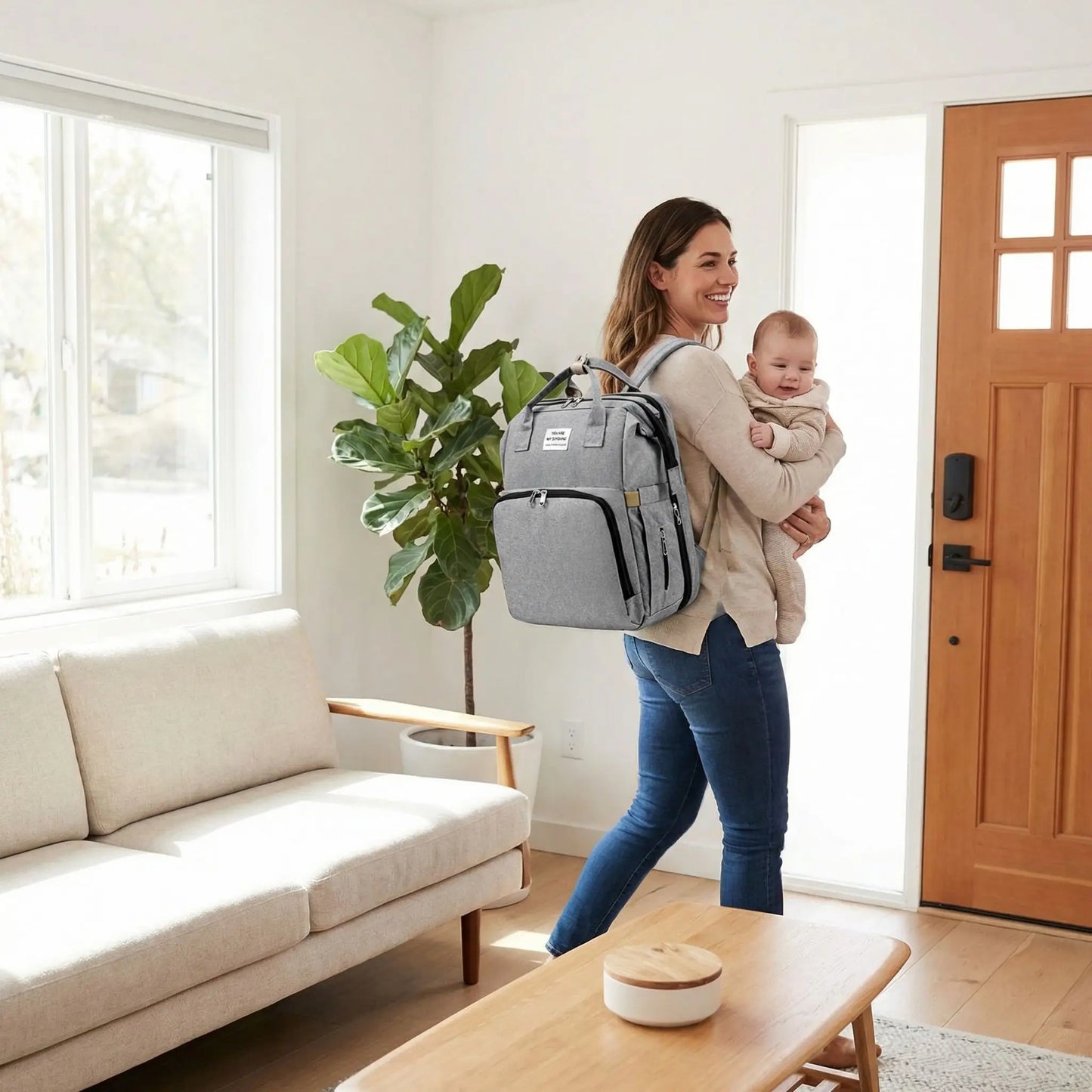 Sac a dos a langer bebe gris porte par une maman quittant la maison avec son enfant dans les bras
