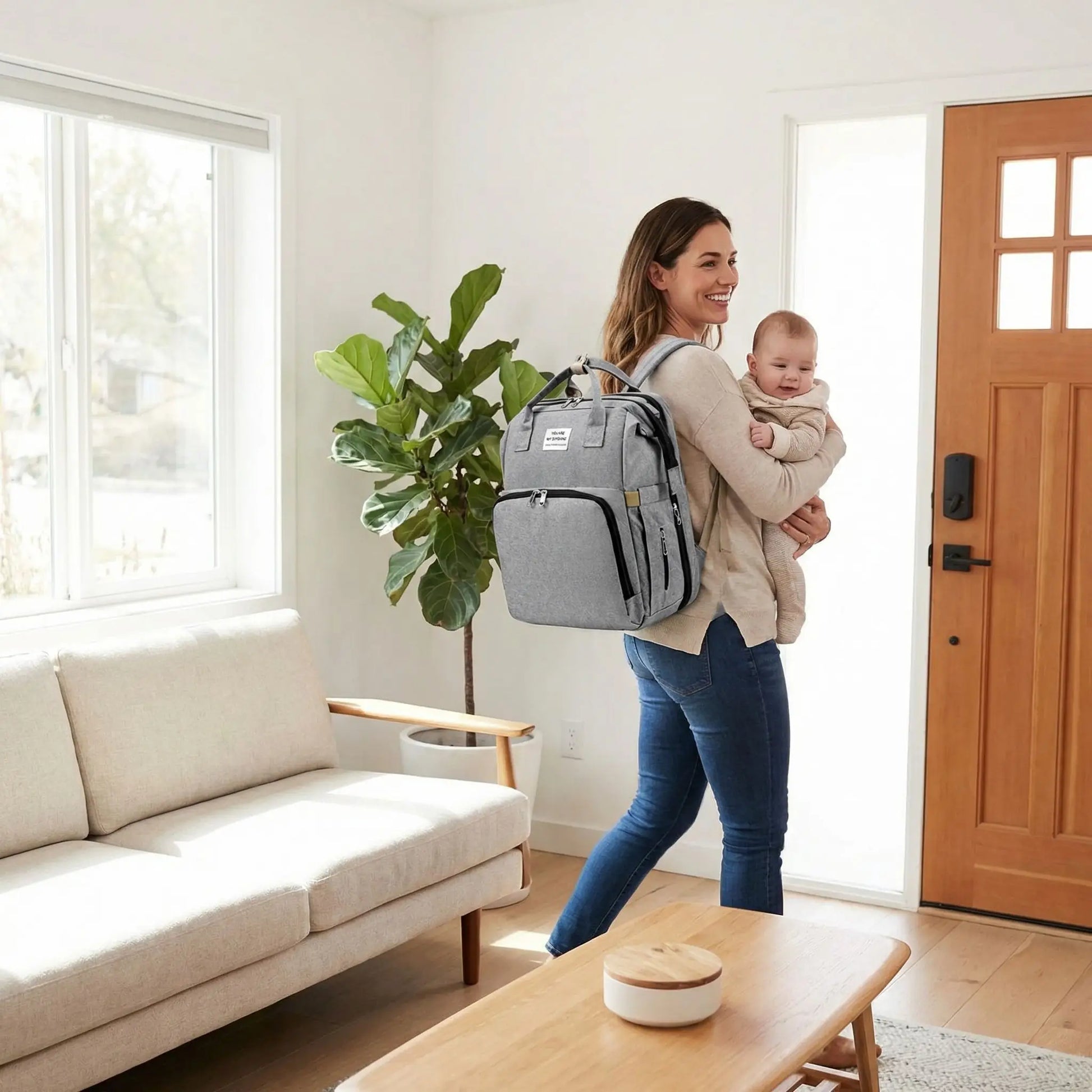 Sac a dos a langer bebe gris porte par une maman quittant la maison avec son enfant dans les bras