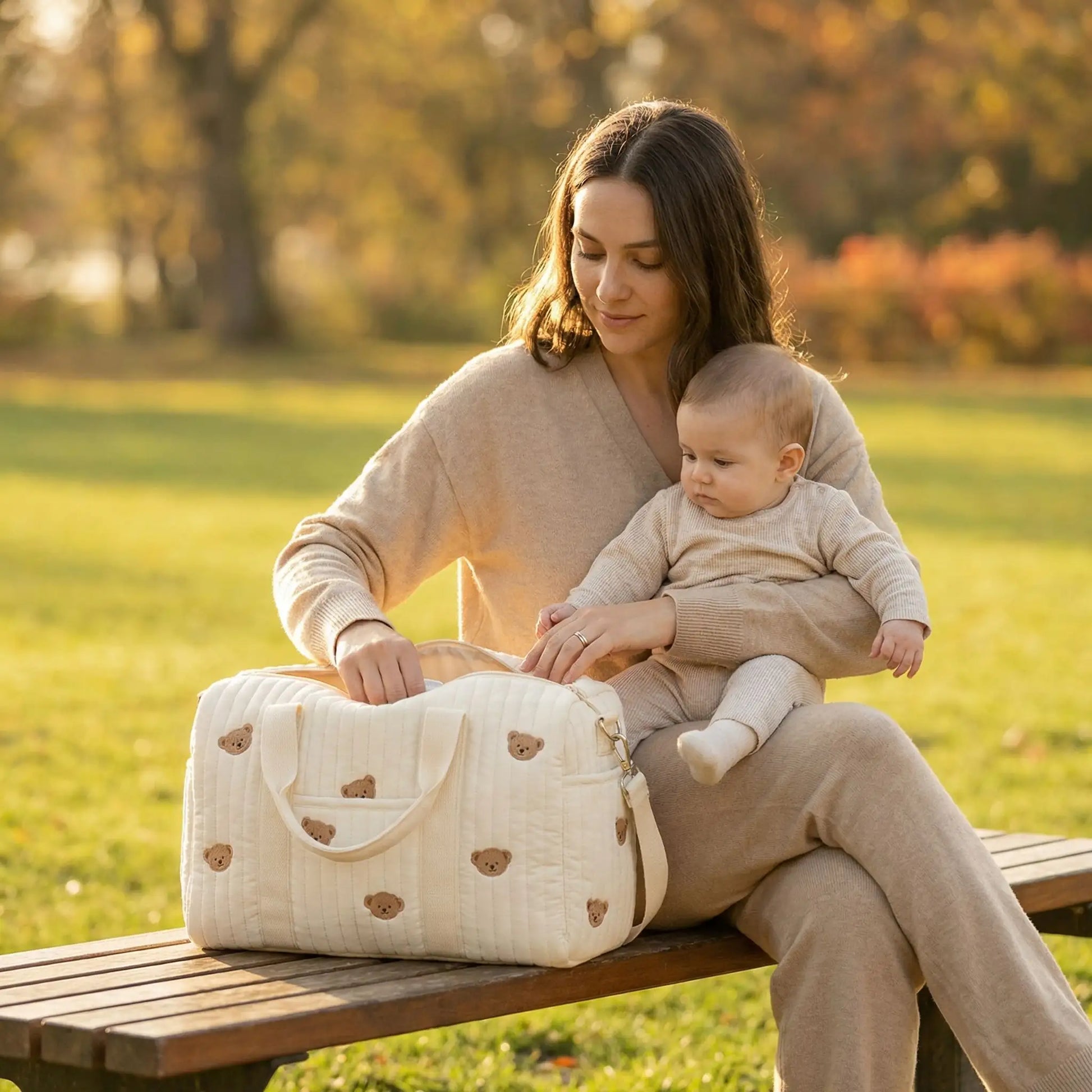 maman assise au parc prend un jouet  dans son sac a langer bebe legerement ouvert