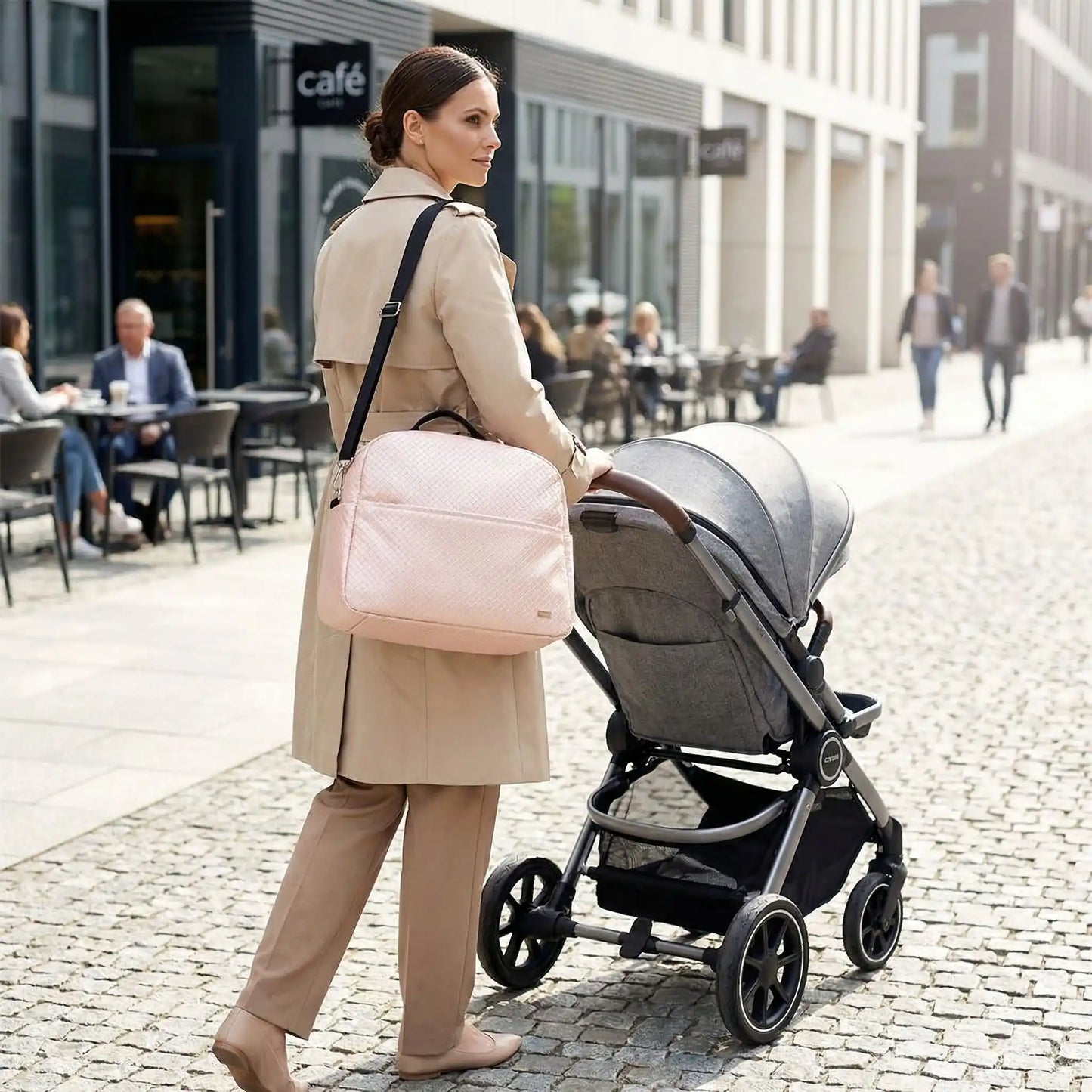 sac a langer beige porte a lepaule par une maman marchant dans une rue pietonne avec poussette
